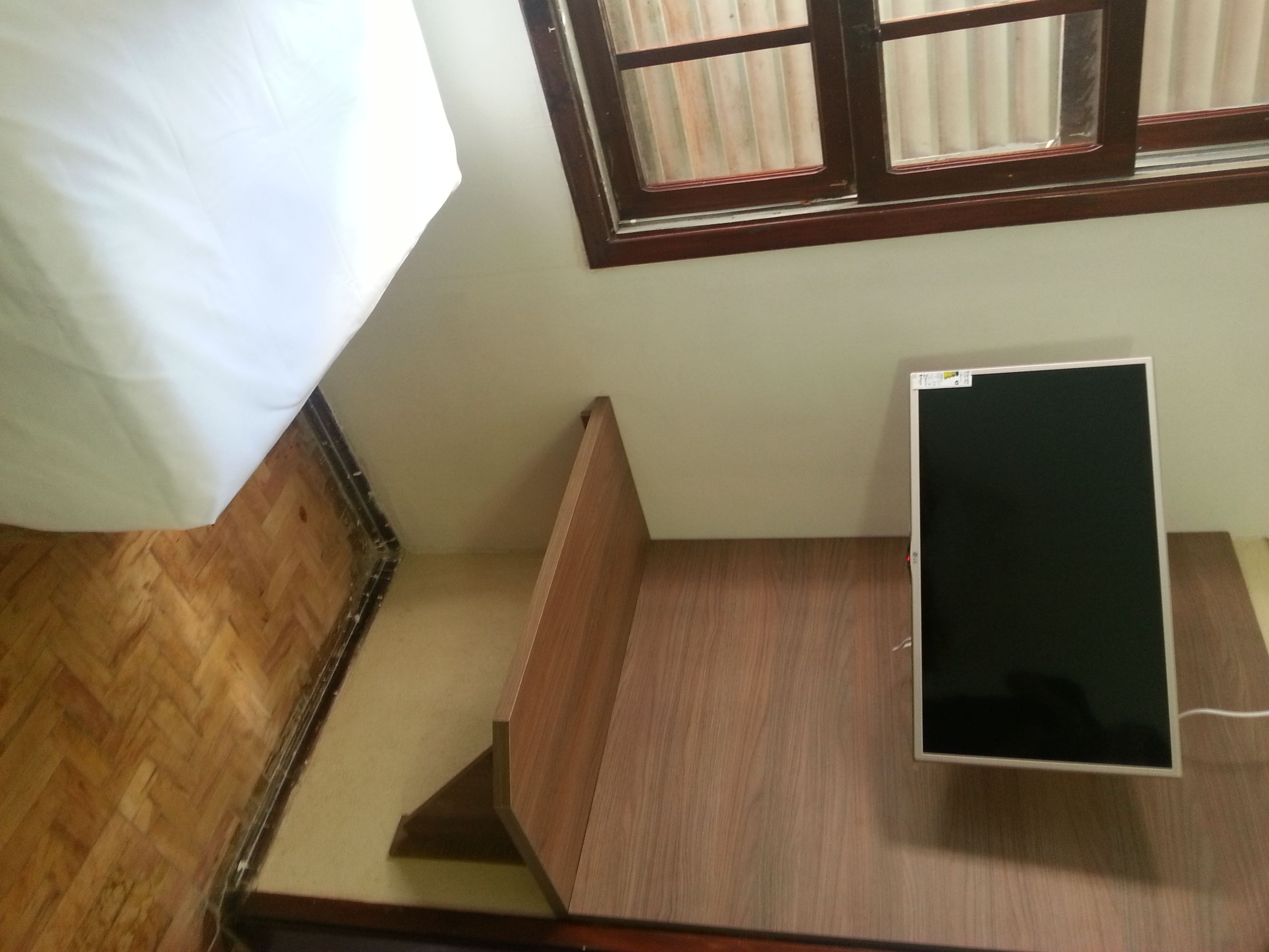 A room with a bed, a wooden desk, and a window with blinds.