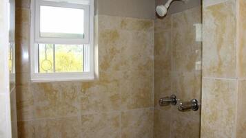 A bathroom with beige tiles, a window, and a shower with a handheld showerhead.