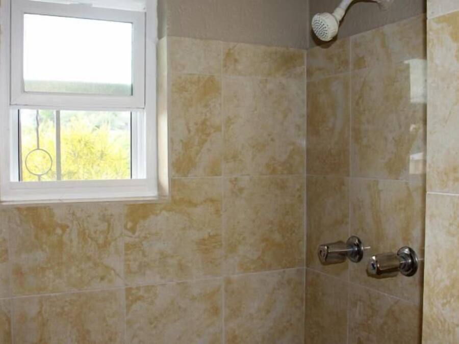 A bathroom with beige tiles, a window, and a shower with a handheld showerhead.