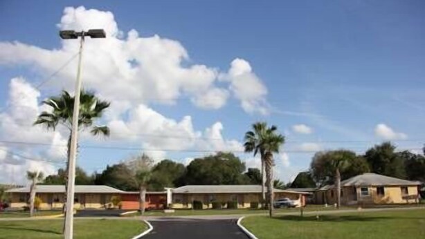 A pathway leading to a row of single-story buildings with a clear sky and palm trees.