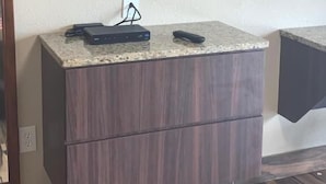 A flat-screen TV mounted on a wall above a wooden cabinet with a countertop.