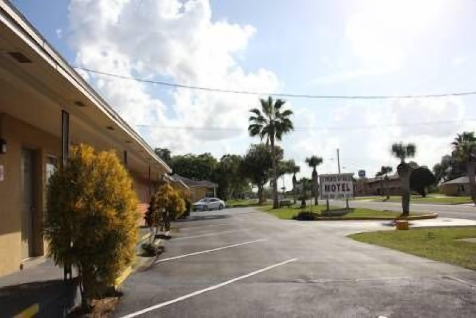 A motel with a parking lot, palm trees, and a clear sky.