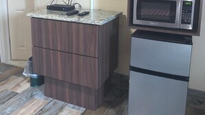 A kitchenette with a microwave, a small refrigerator, and a flat-screen TV mounted on the wall.