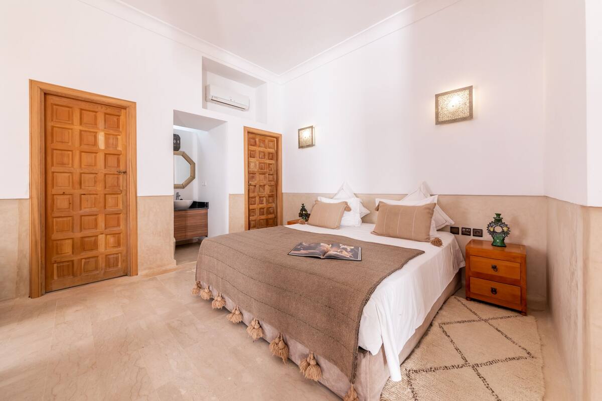 A bedroom with a large bed, wooden doors, a nightstand, and a wall-mounted light fixture.