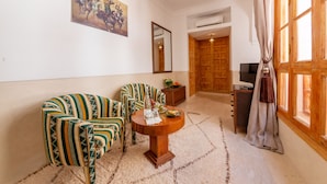 Quarto com sofá, cadeiras, mesa redonda, quadro, espelho, televisão e porta de madeira.