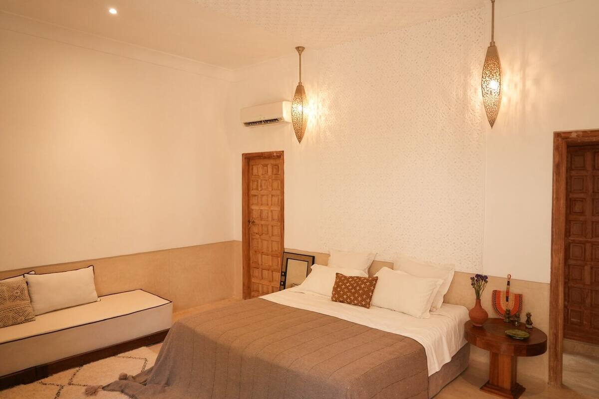 A bedroom with a bed, a sofa, a nightstand, and a wall-mounted air conditioner.