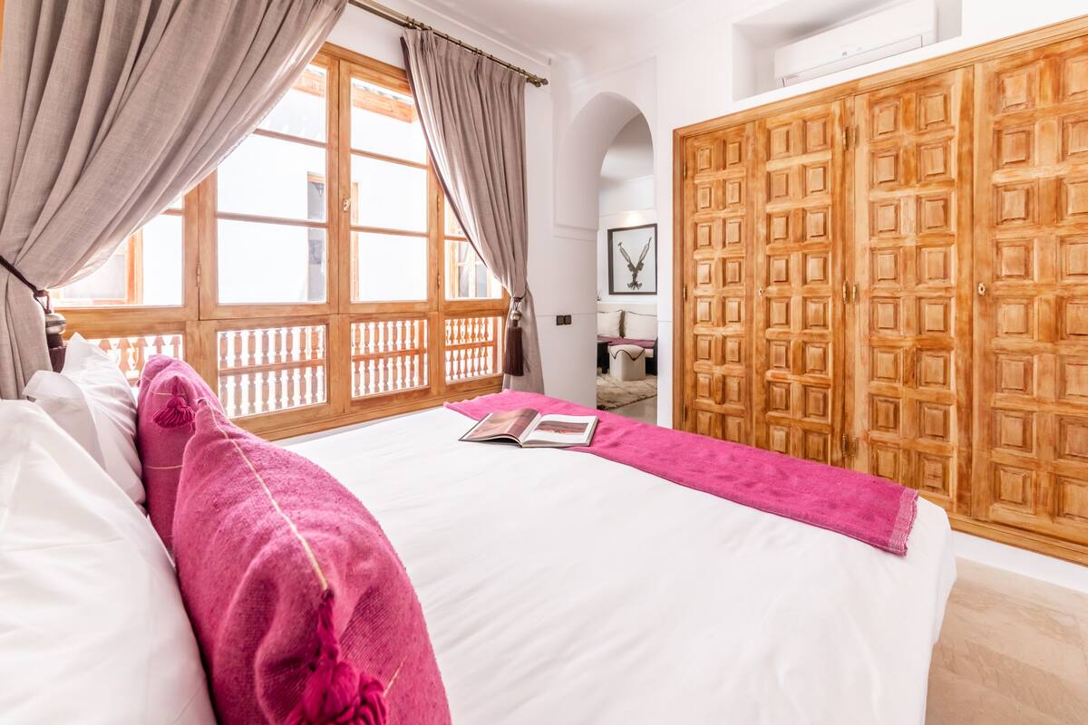 A bedroom with a large bed, a wooden wardrobe, and a window with curtains.