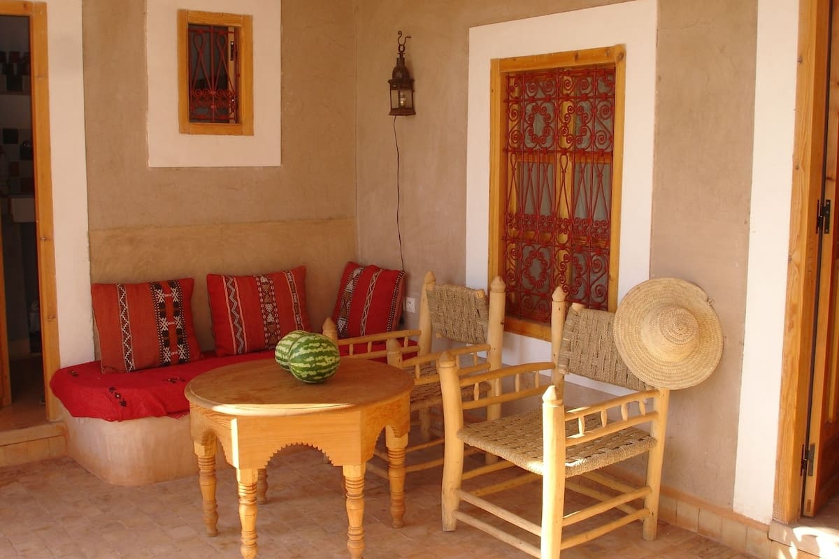 A cozy seating area with a wooden table, two chairs, and a sofa with patterned cushions.