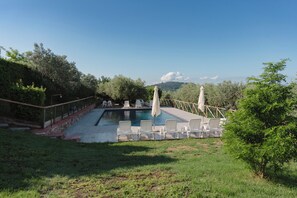 A swimming pool with lounge chairs and umbrellas, surrounded by greenery and hills in the background.
