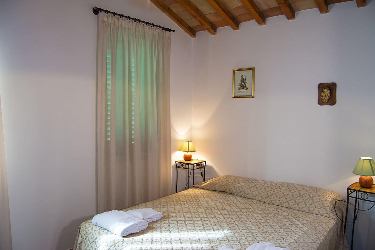Un dormitorio con una cama, dos mesitas de noche, una ventana con cortinas y techo de madera.