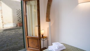 Ein Zimmer mit Holztür, einem kleinen Nachttisch mit Lampe und einem Bett mit grüner Bettdecke.
