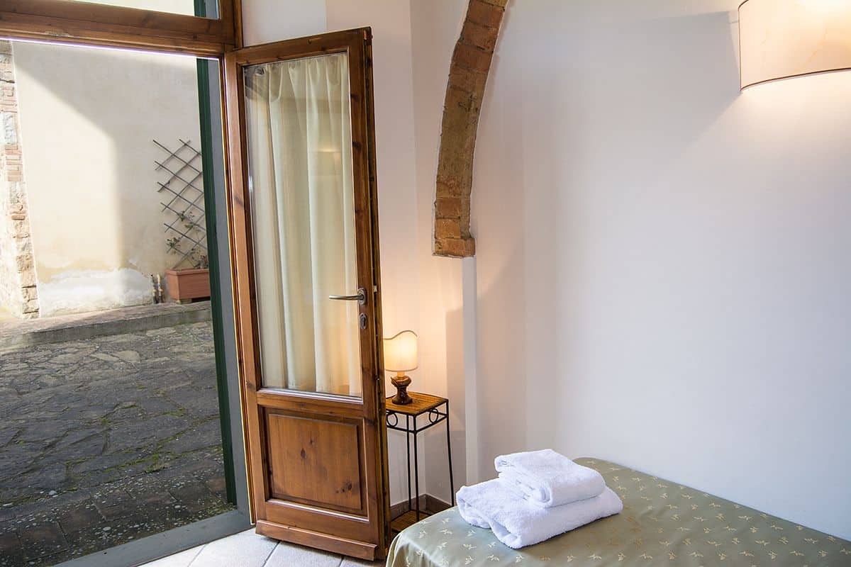 Una habitación con una puerta de madera, una mesita de noche pequeña con una lámpara, y una cama con colcha verde.