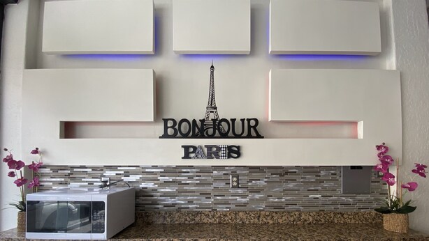 A reception desk with a sign reading "BONJOUR PARIS" and decorative elements including a model of the Eiffel Tower and orchid plants. - Hotel Paris (Tijuana)
