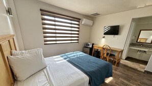 A bedroom with a bed, a desk, a chair, a TV, and a bathroom. - Hotel Paris (Tijuana)