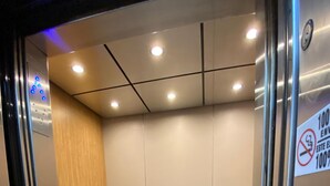 An elevator interior with a wooden panel on one side, a metal handrail, and a sign indicating a 100% non-smoking policy. - Hotel Paris (Tijuana)