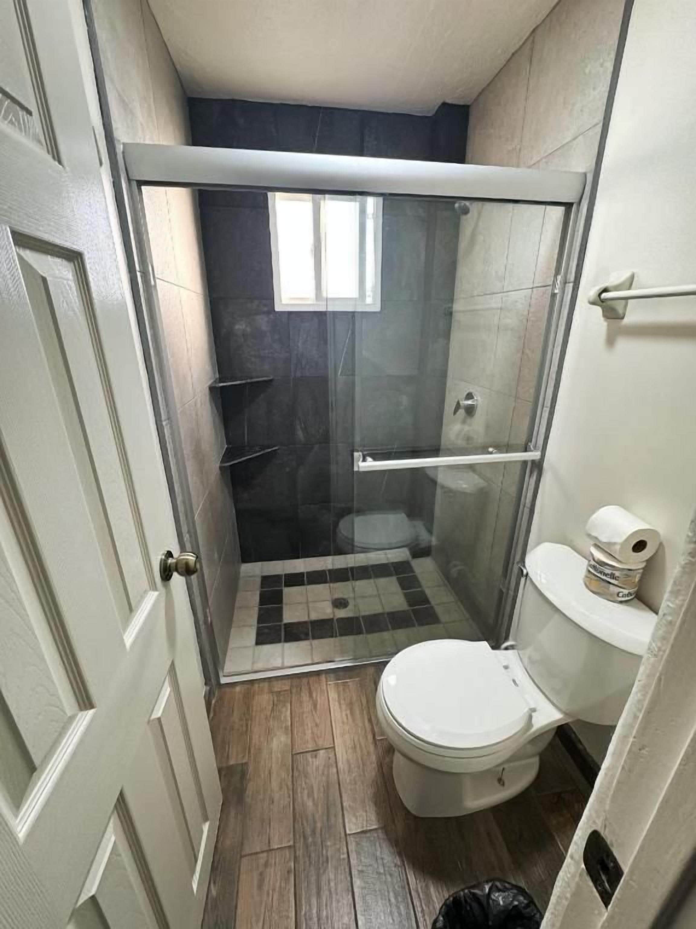 Un baño con ducha envuelta en vidrio, inodoro y puerta.