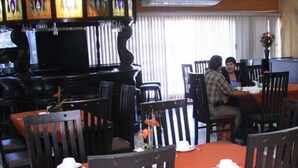 A restaurant with wooden chairs and tables, a bar area, and a window with blinds. - Hotel Yori (Cajeme)