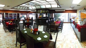 A dining area with multiple tables set for service, a central bar, and a view of the outdoors. - Hotel Yori (Cajeme)