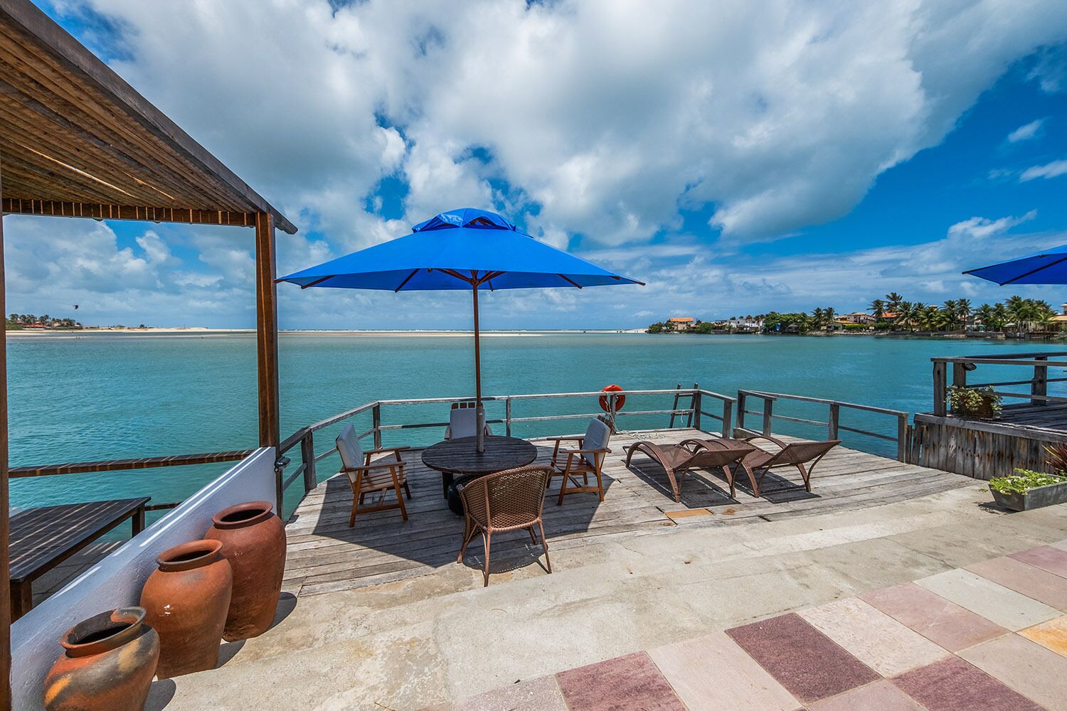 A wooden deck with outdoor seating, overlooking a calm sea and a distant shoreline.