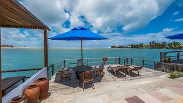 A wooden deck with outdoor seating, overlooking a calm sea and a distant shoreline.