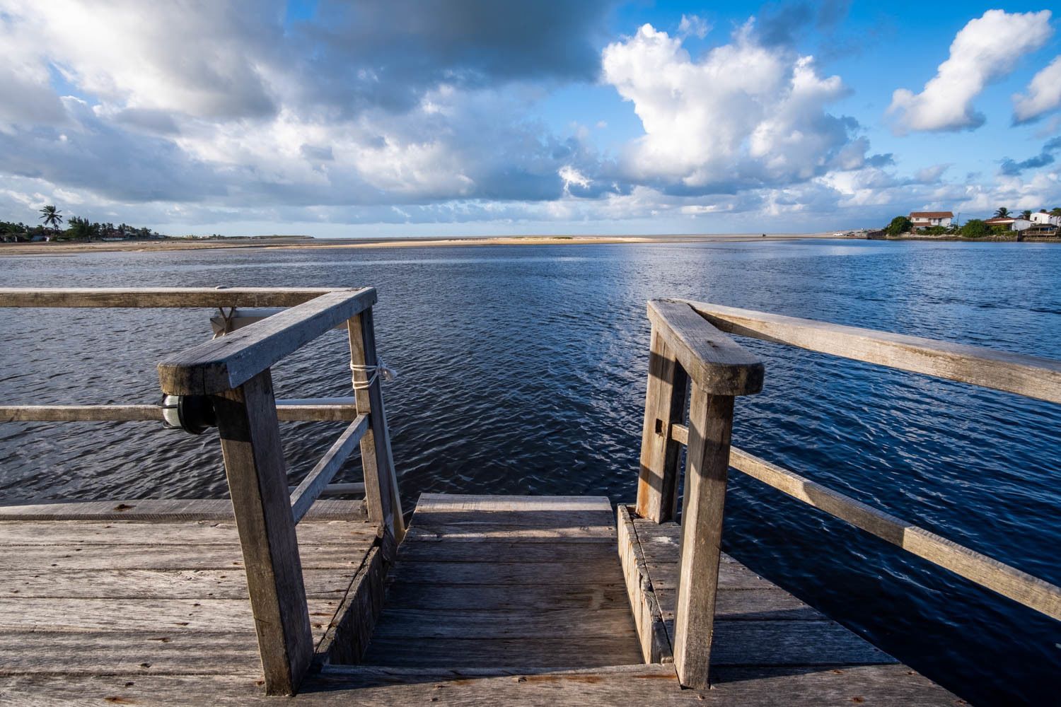 A wooden pier leading into calm waters with a clear sky.