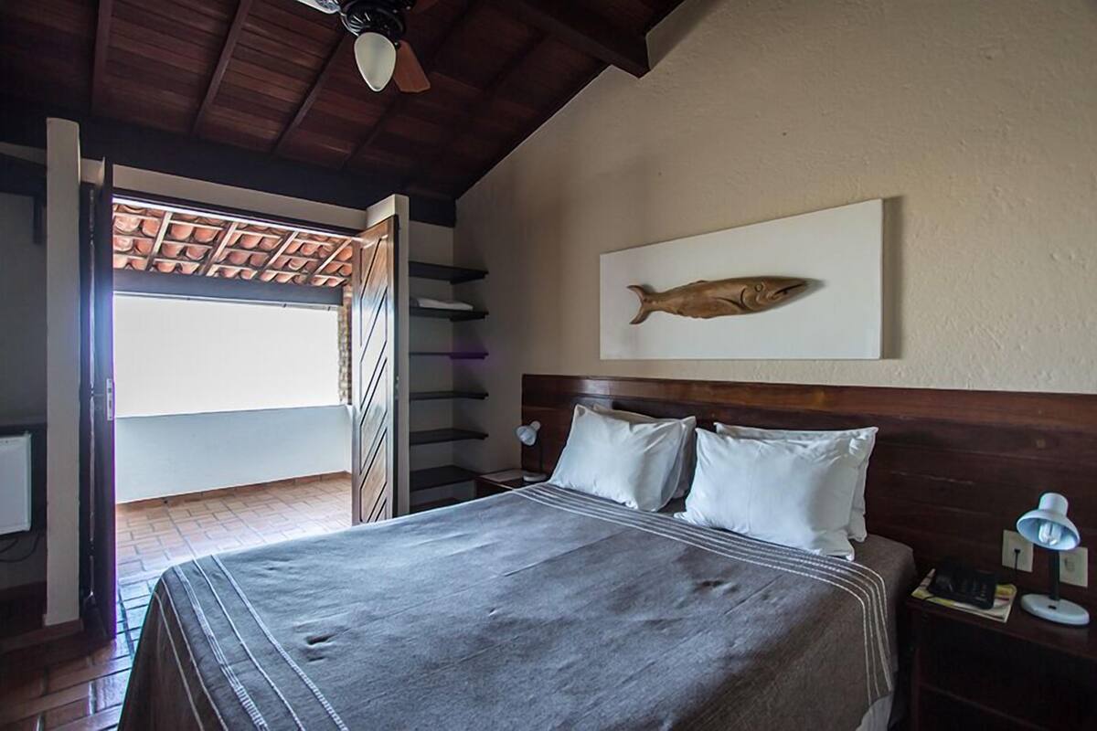 Un dormitorio con cama, mesita de noche, lámpara, una obra de arte de peces en la pared y vistas al exterior a través de una puerta abierta.