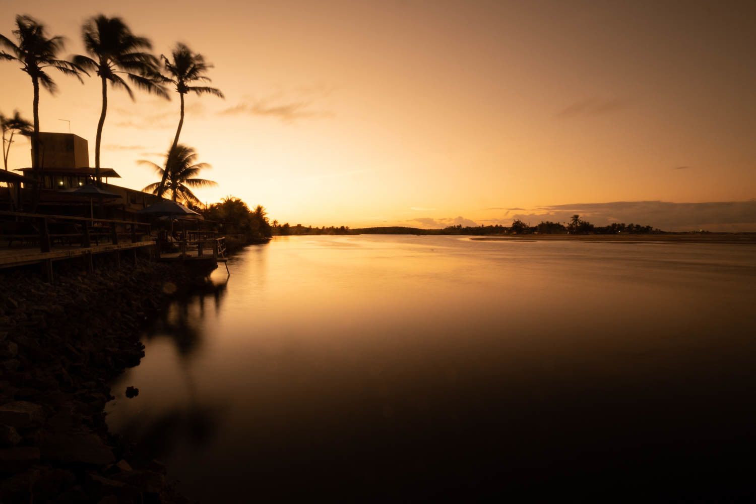 A waterfront property with a long pier, palm trees, and a sunset.