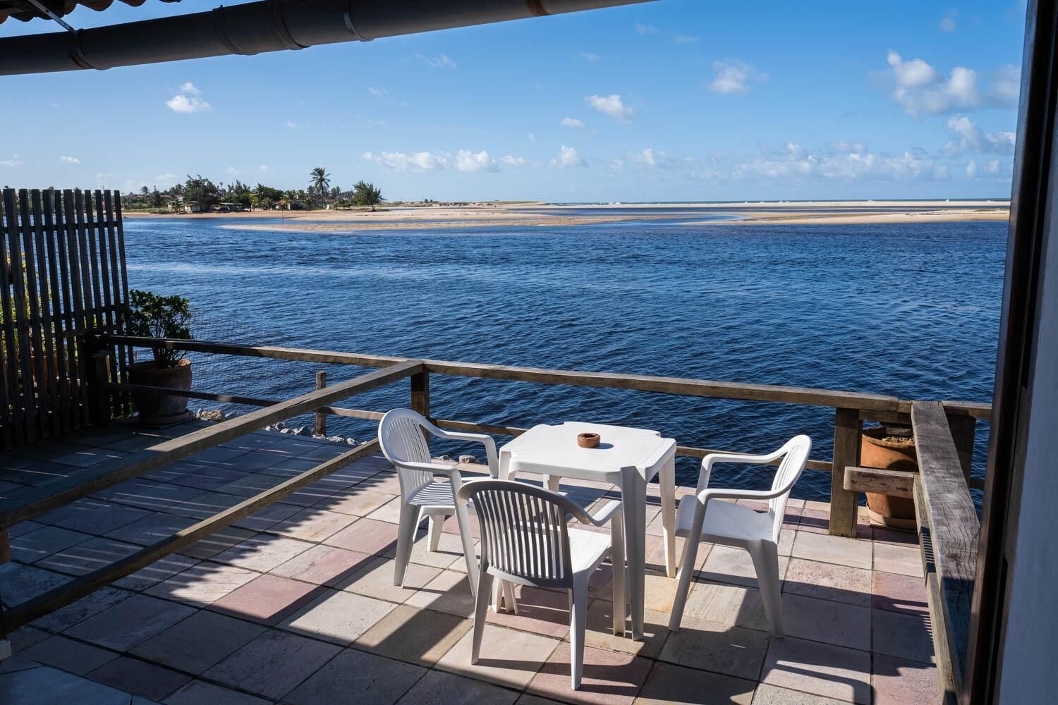A terrace with a table and chairs overlooking a beach and the sea.