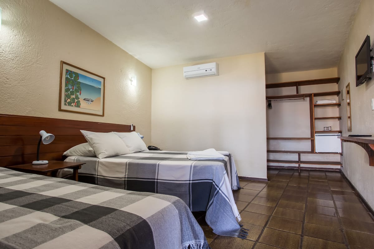 Habitación de hotel con dos camas, un escritorio con lámpara, un cuadro en la pared y un armario empotrado.