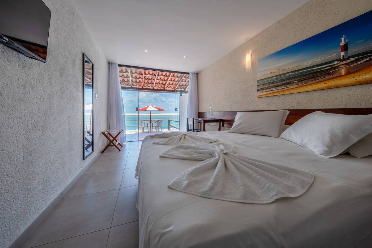Habitación de hotel con una cama grande, un cuadro de un faro y vista al océano a través de una puerta de vidrio.