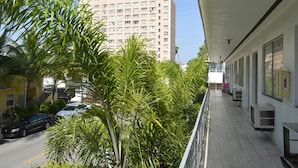 A balcony with a view of a tall building, palm trees, and parked cars. - Art Deco Ocean Walk Apartments (Miami Beach)