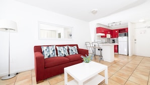 A modern living room with a red sofa, a white coffee table, and a kitchen area with red cabinets and white appliances. - Art Deco Ocean Walk Apartments (Miami Beach)