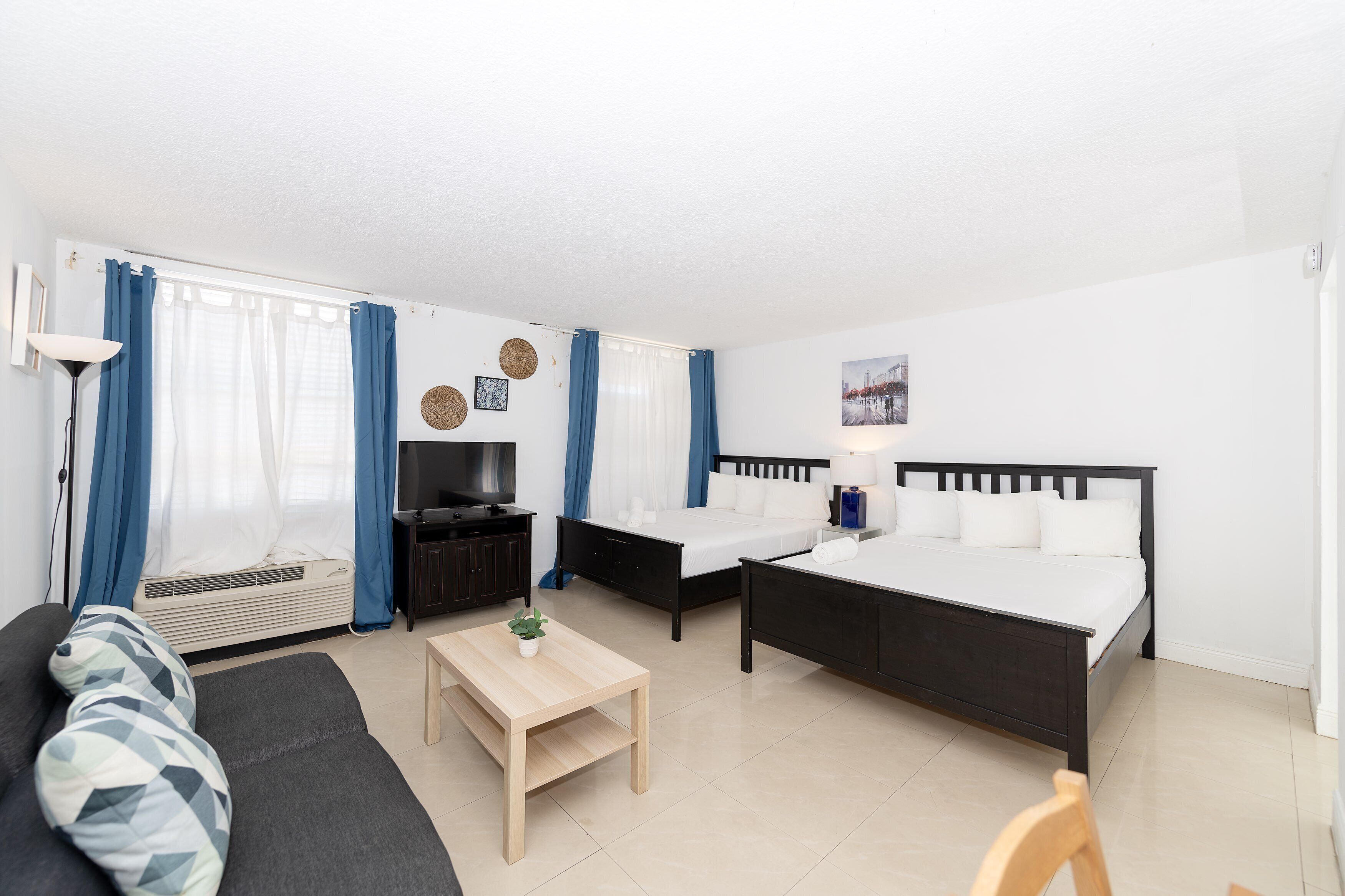 Quarto de hotel moderno com sofá, duas camas, uma TV e uma pequena mesa.