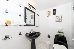 Ein modernes Badezimmer mit einem schwarzen Waschbecken, einem großen Spiegel und einer Toilette. An den Wänden befinden sich Bilder in Rahmen, und ein Ablagefach beherbergt Toilettenartikel.