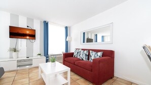 A modern living room with a red sofa, white coffee table, and a flat-screen TV mounted on the wall. - Art Deco Ocean Walk Apartments (Miami Beach)