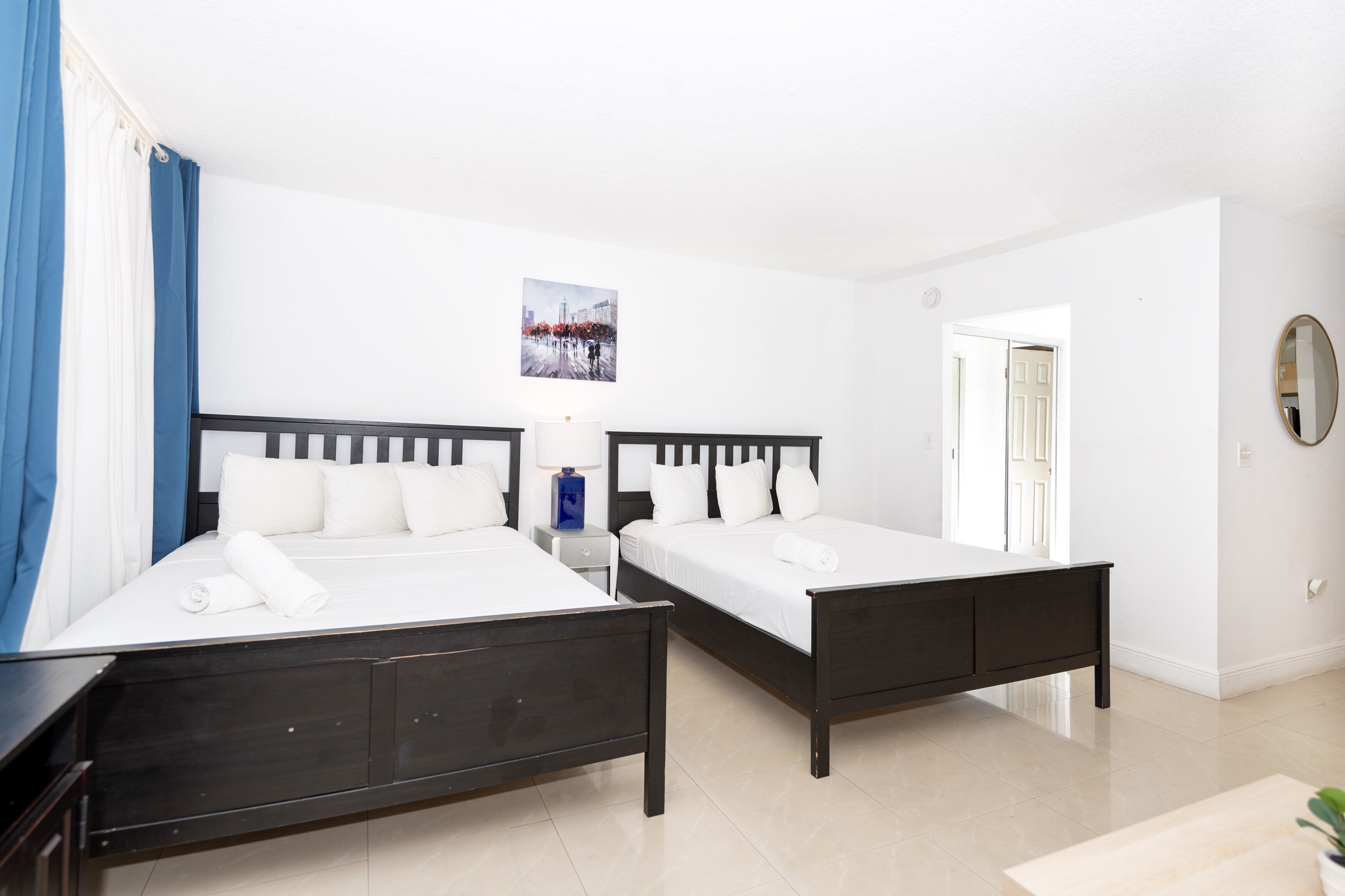 A hotel room with two beds, a nightstand, a lamp, and a painting on the wall.