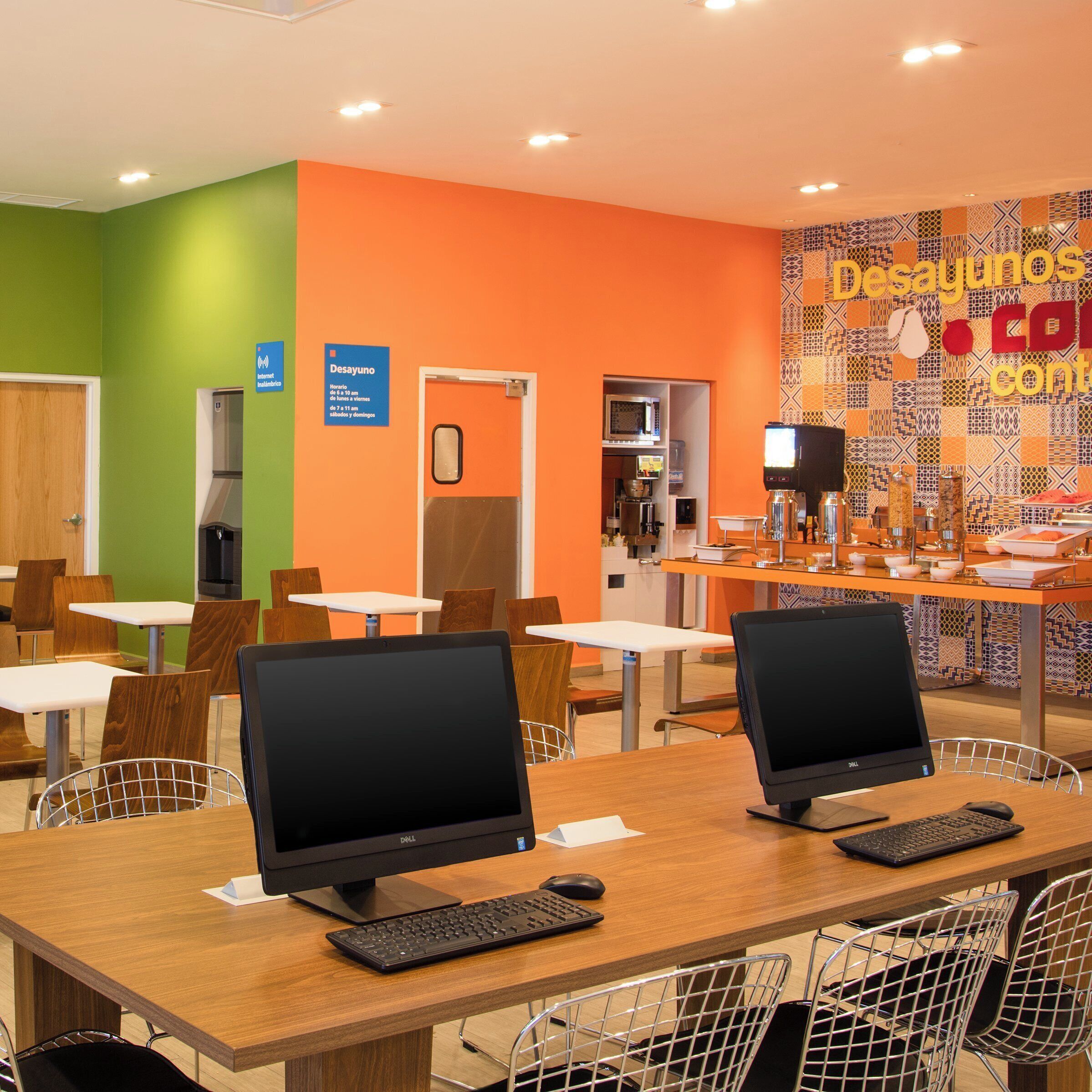 Un café moderne doté de nombreuses tables, chaises et ordinateurs. Des panneaux indiquent qu’il s’agit d’un café et d’un restaurant.