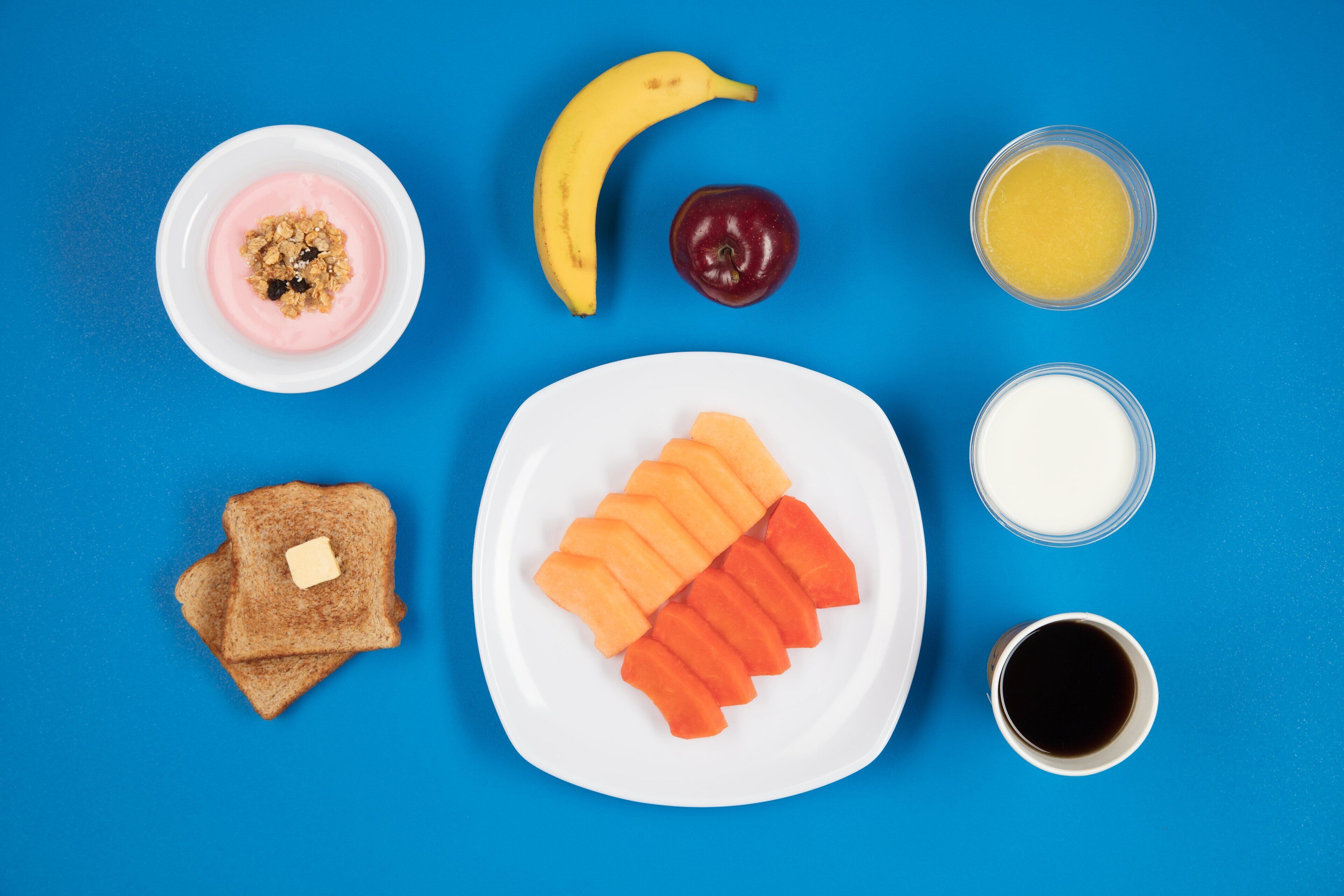Un plato de desayuno con tostadas, plátano, manzana, jugo de naranja, leche y café.