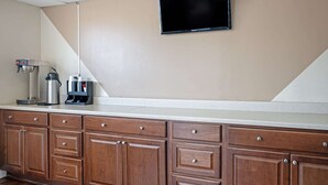 A kitchenette with a coffee maker, a water dispenser, and a flat-screen TV mounted on the wall. - Rodeway Inn Terre Haute near University (Terre Haute)