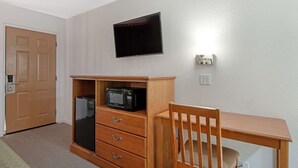 A room with a wooden desk, a television mounted on the wall, a microwave on a cabinet, and a door. - Rodeway Inn Terre Haute near University (Terre Haute)