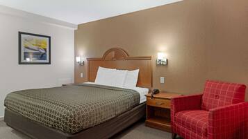 Een hotelkamer met een groot bed, een houten hoofdbord, een rode fauteuil en een lijst met een afbeelding aan de muur.