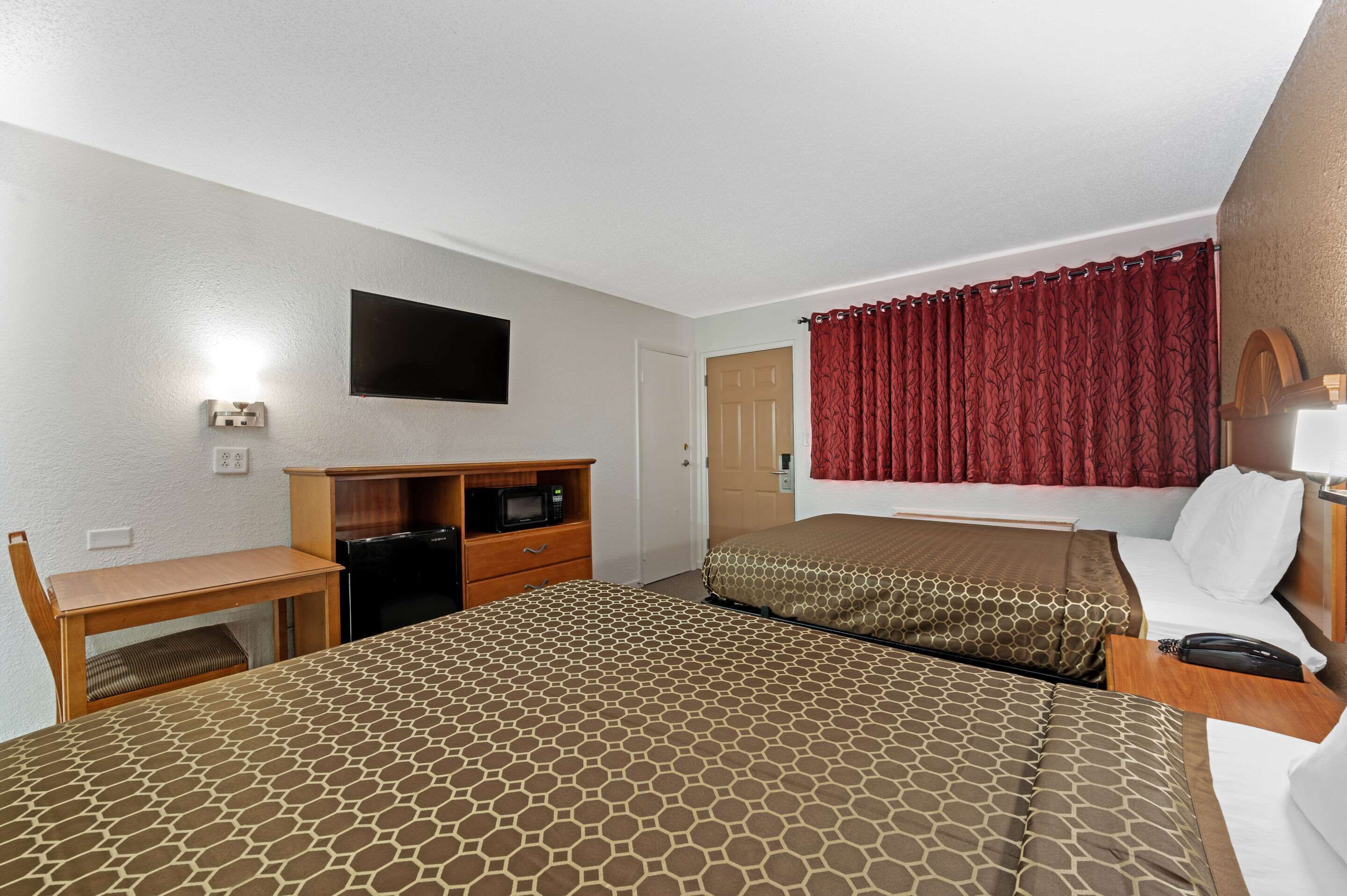 Habitación de hotel con dos camas, un escritorio con microondas, televisión y cortina roja.