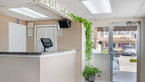 A reception area with a counter, a computer monitor, a door, and a view of the street outside. - Rodeway Inn Terre Haute near University (Terre Haute)