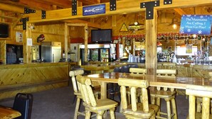 Un interior rústico de madera con techos altos, una zona de bar y mesas y sillas de madera.