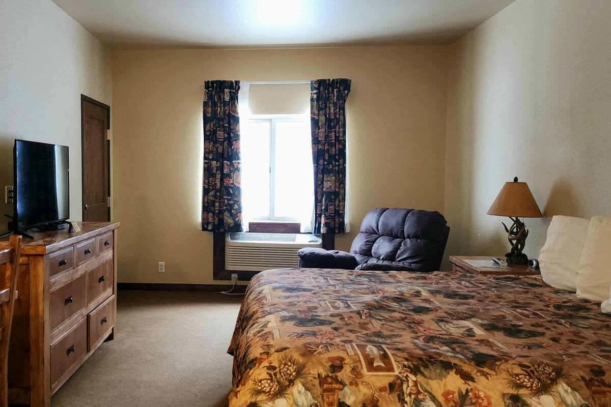 Quarto com cama, penteadeira, cadeira, luminária e janela com cortinas.