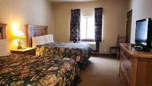 Una habitación de hotel con dos camas, televisión, escritorio con cajones, una silla y ventana con cortinas.