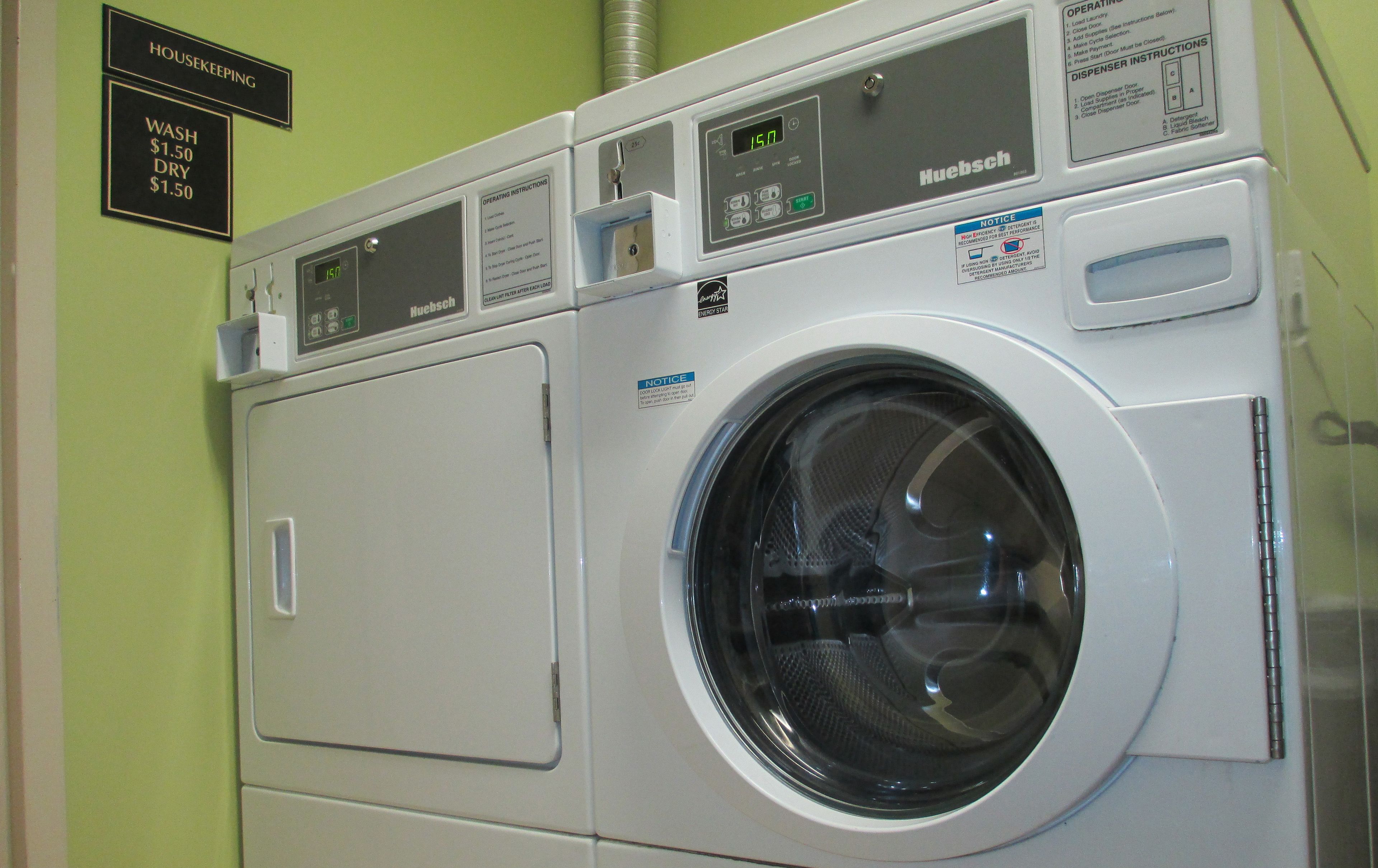 Une machine à laver Huebsch à chargement frontal, dotée d’un écran numérique, d’un manuel d’utilisation et d’une étiquette indiquant le prix des services de lavage et de séchage.