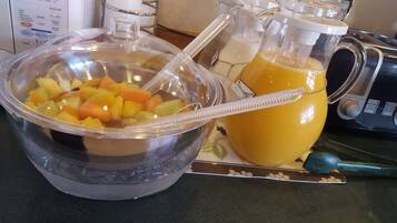 Una encimera de cocina con un frutero con frutas cortadas, una jarra de zumo de naranja y una licuadora.