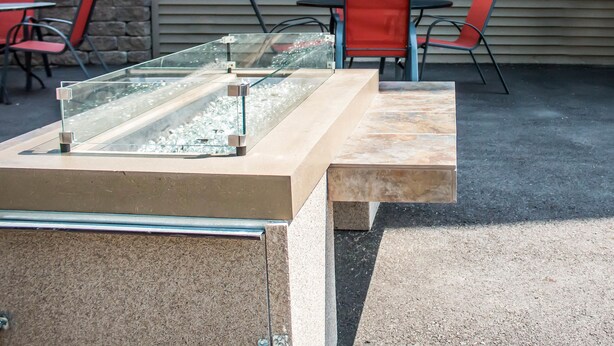Un espace patio avec une table et des chaises à plateau en verre, un banc en pierre et un mur de pierre en arrière-plan.