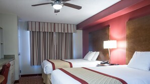 Une chambre d’hôtel avec deux lits, un bureau, une chaise, un ventilateur de plafond et une fenêtre avec des rideaux.